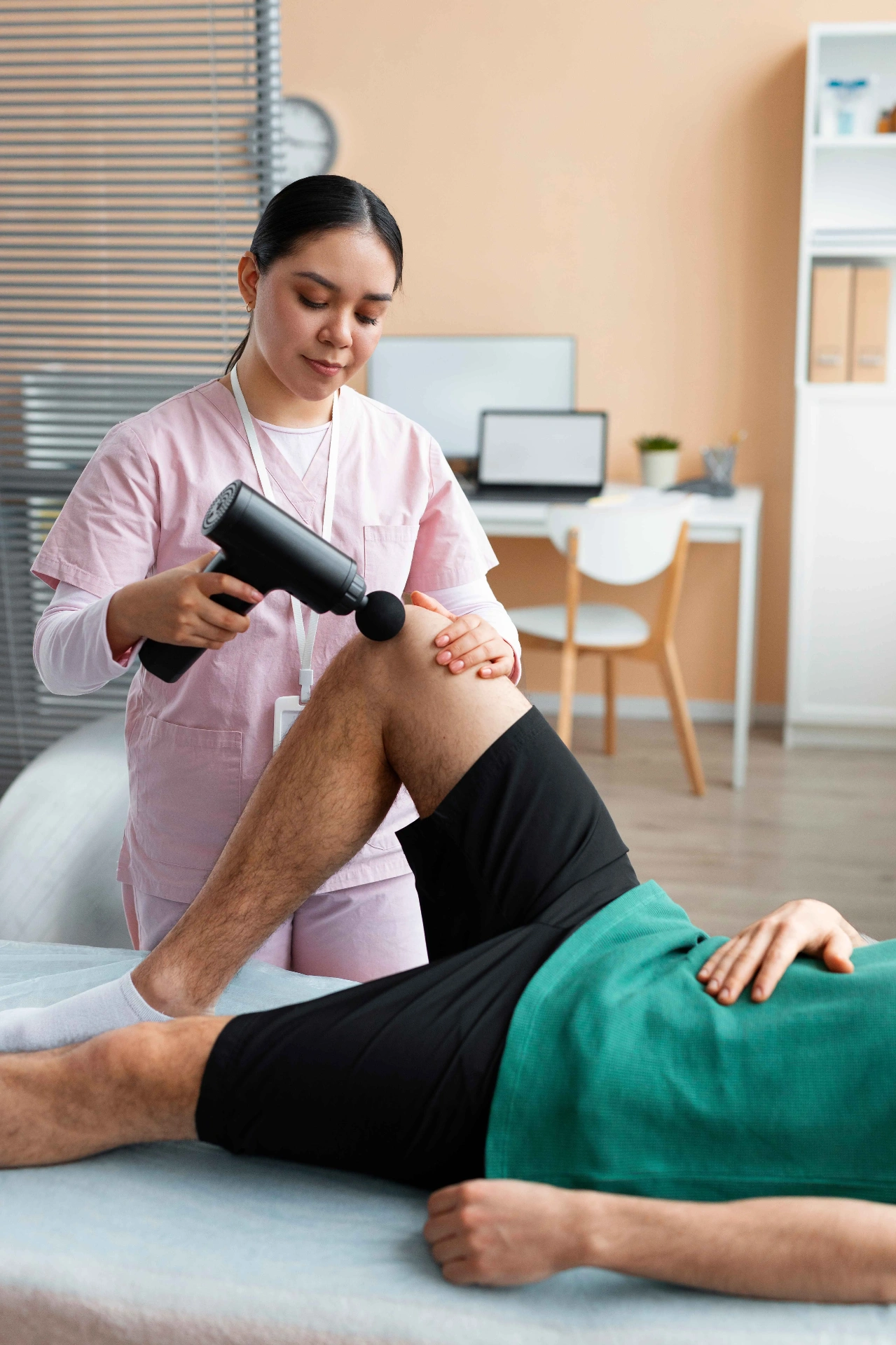 Fisioterapeuta aplicando massagem terapêutica com pistola de percussão no joelho de paciente em sessão de fisioterapia traumato-ortopédica em Curitiba
