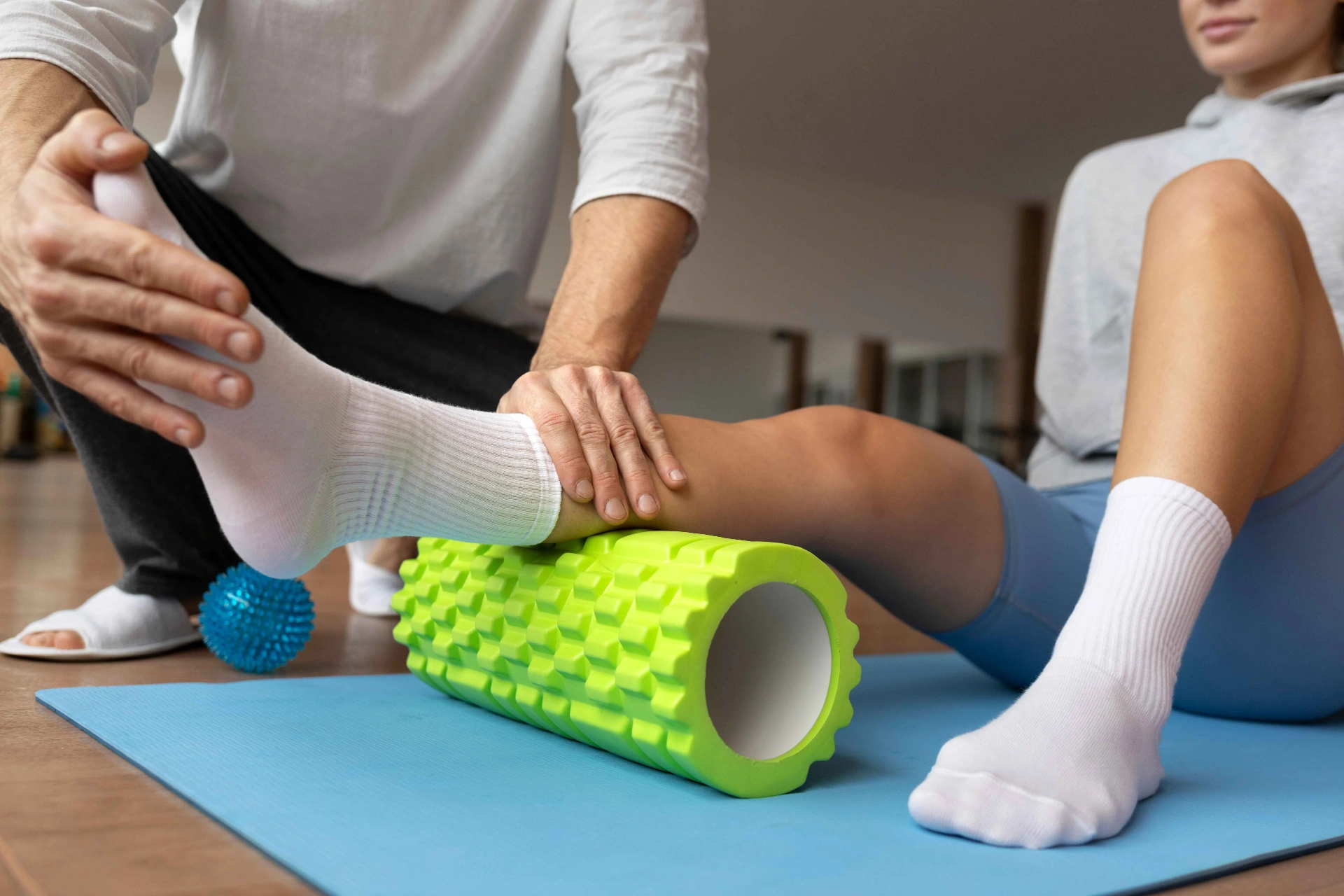 Fisioterapeuta utilizando rolo de liberação miofascial e bola de massagem na reabilitação ortopédica do tornozelo de paciente em Curitiba